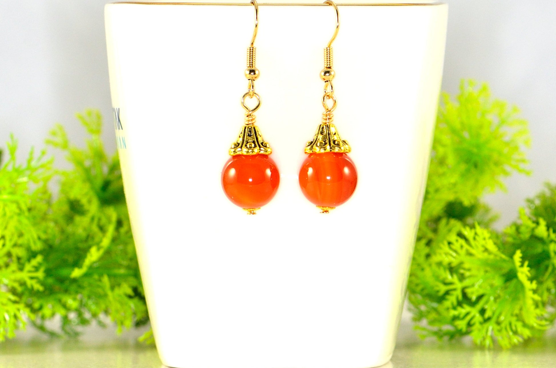 12mm Natural Carnelian Crystal Drop Earrings displayed on a tea cup.