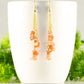 Long Gold Plated Chain and Carnelian Crystal Chip Earrings displayed on a coffee mug.