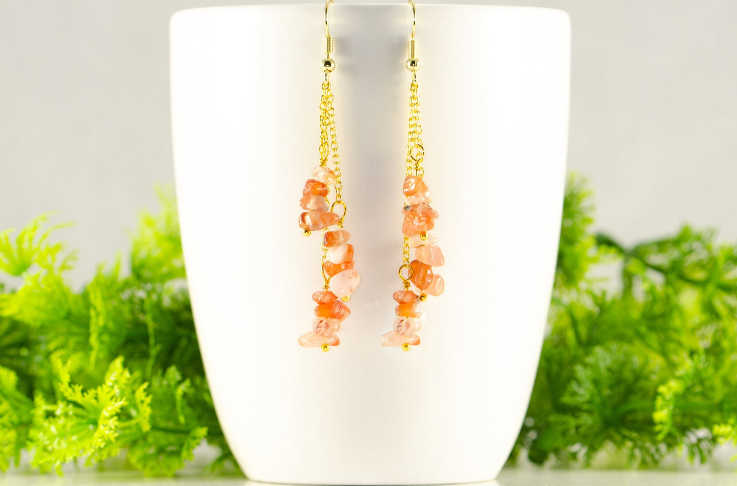 Long Gold Plated Chain and Carnelian Crystal Chip Earrings displayed on a coffee mug.