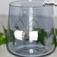 Miniature Toilet Paper Roll Earrings displayed on a glass.