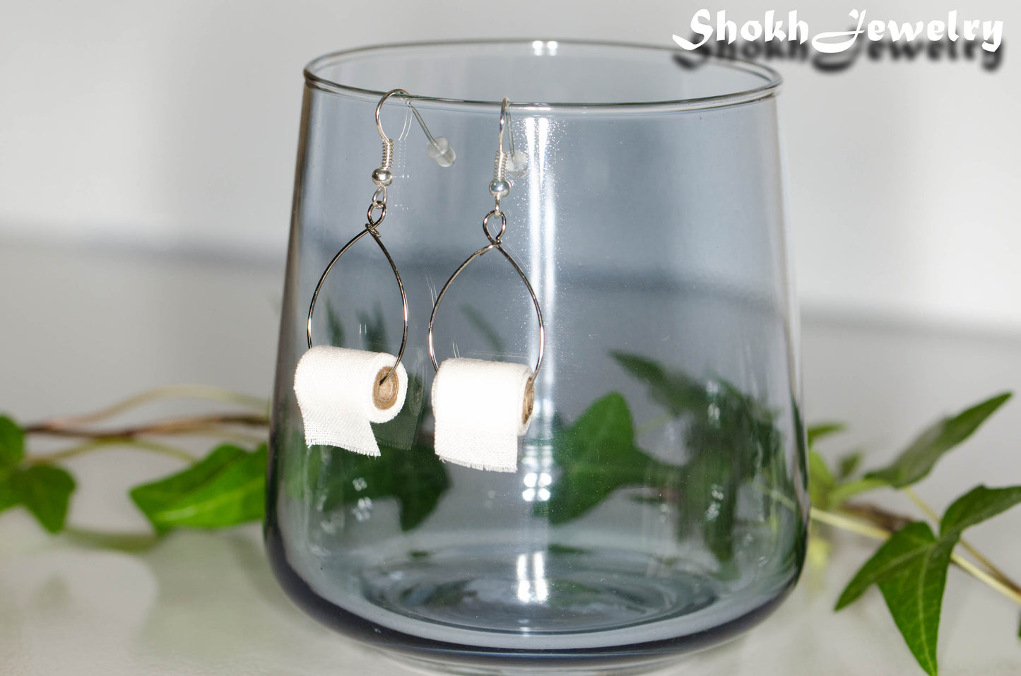 Miniature Toilet Paper Roll Earrings displayed on a glass.
