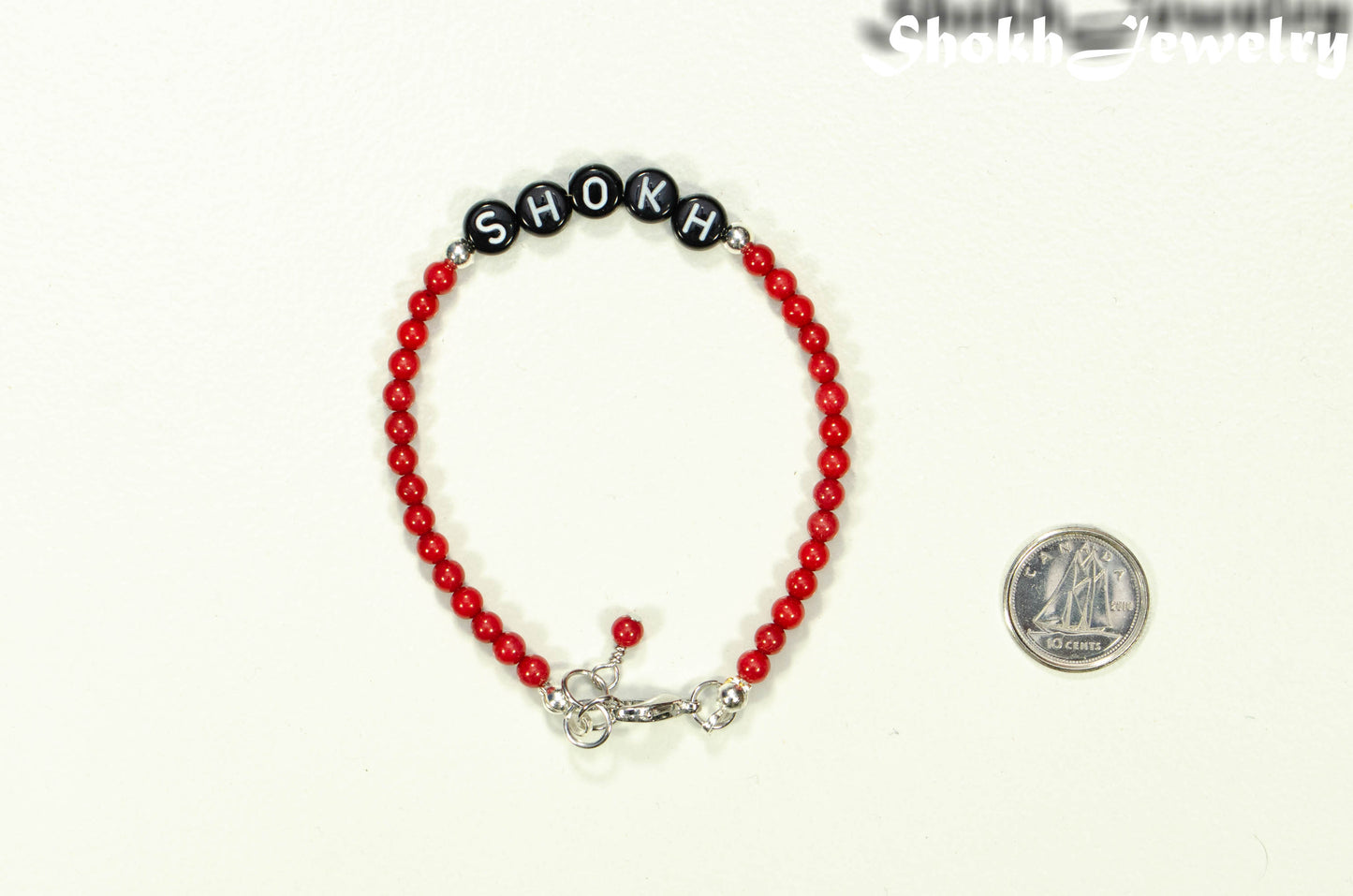 Copy of Personalized Natural Red Coral Name Bracelet with Clasp beside a dime.
