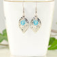 Filigree Leaf Charm and Aqua Blue Glass Crystal Earrings displayed on a tea cup.