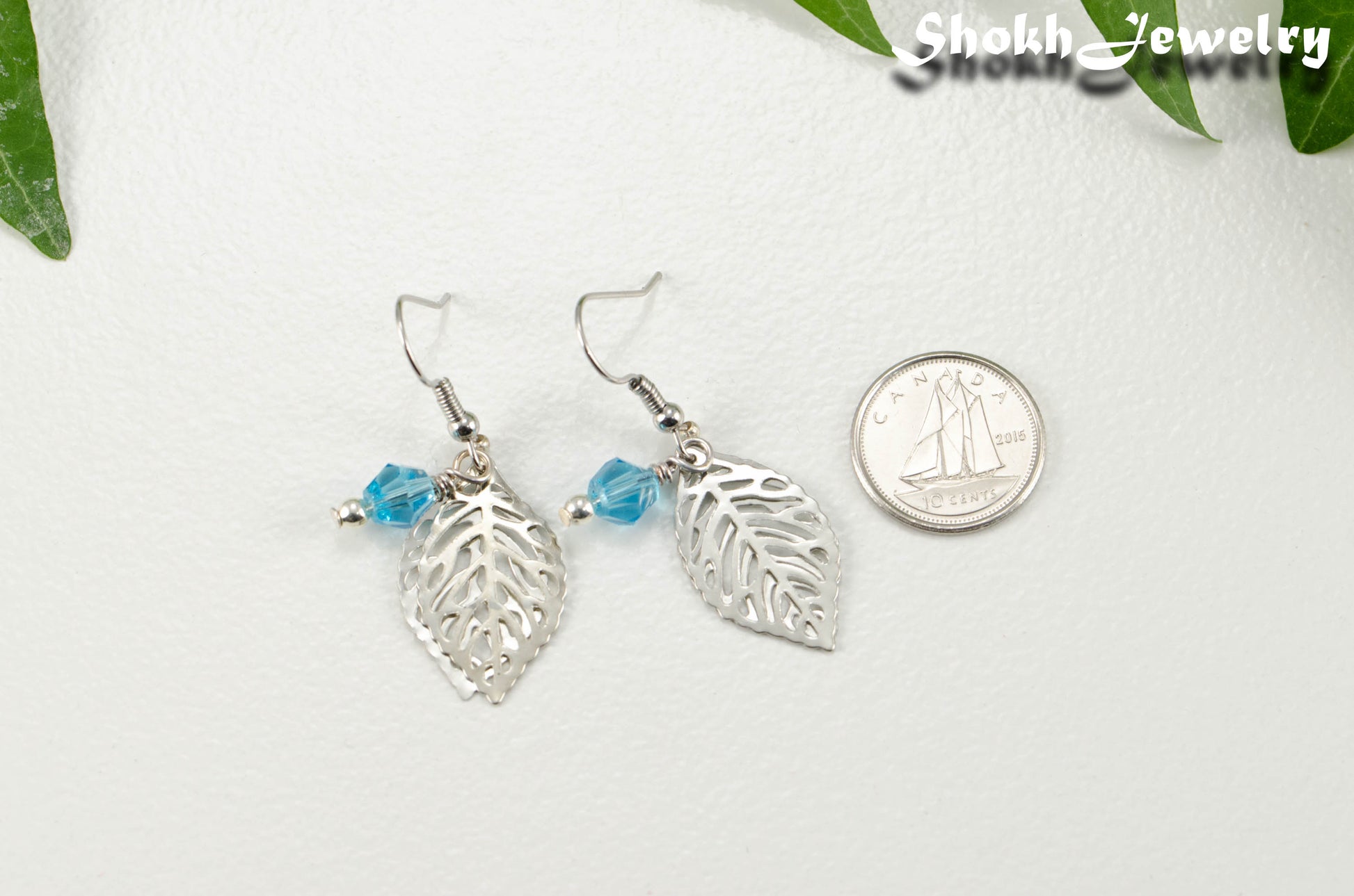 Filigree Leaf Charm and Aqua Blue Glass Crystal Earrings beside a dime.