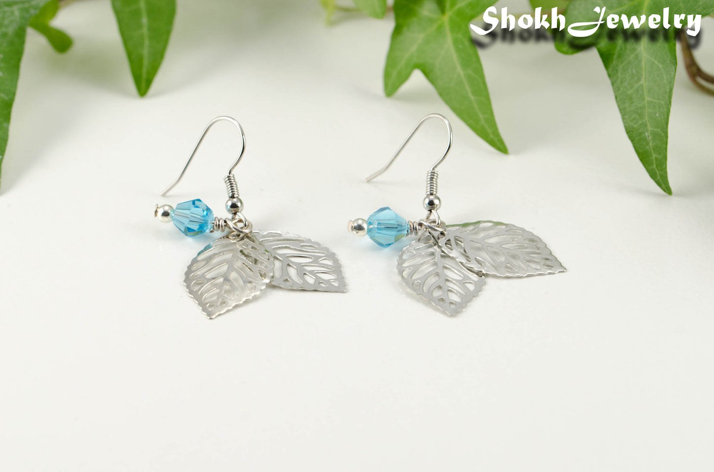 Close up of Filigree Leaf Charm and Aqua Blue Glass Crystal Earrings.
