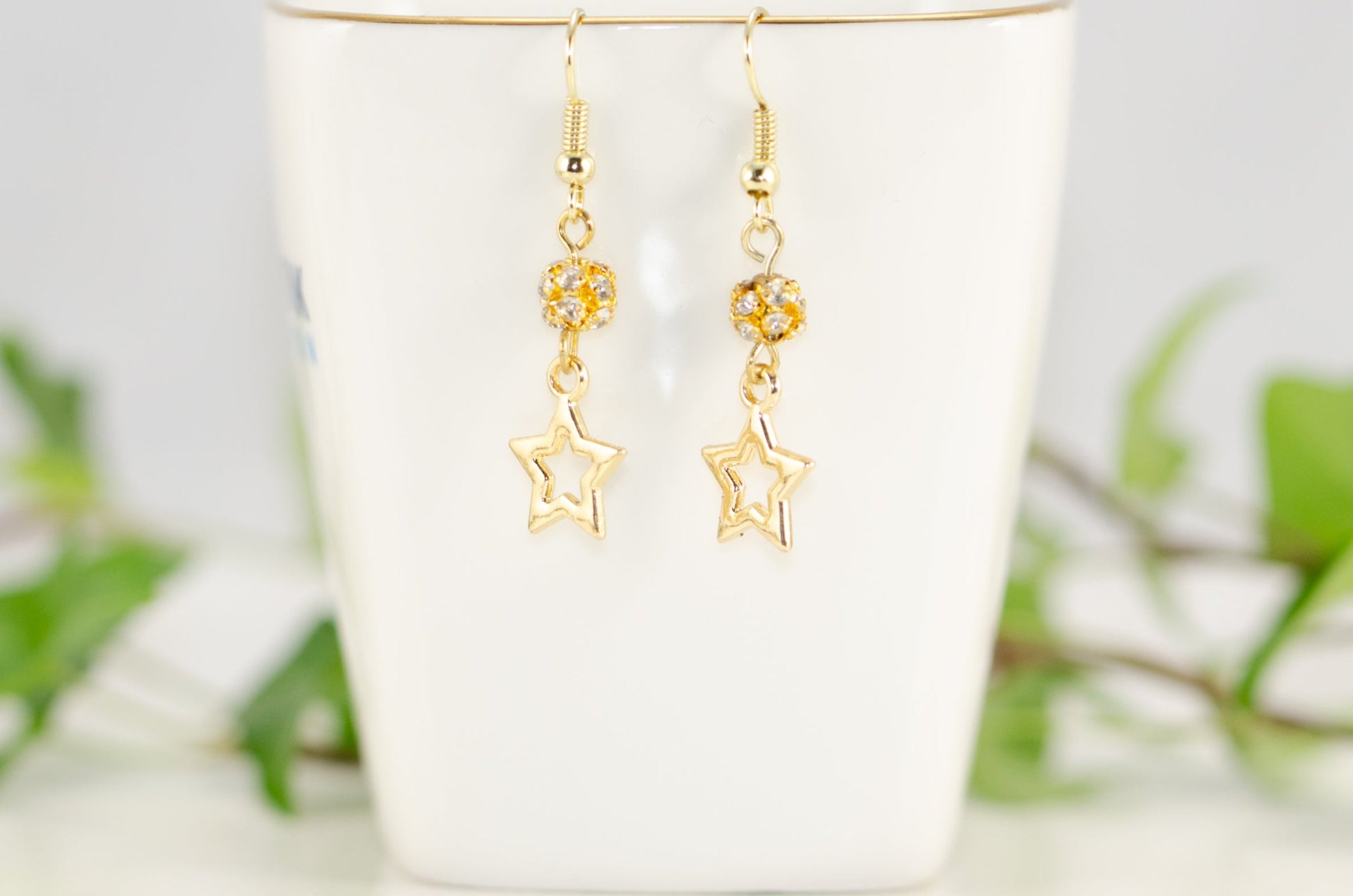 Sparkly Rhinestone and Gold Star Earrings displayed on a tea cup.